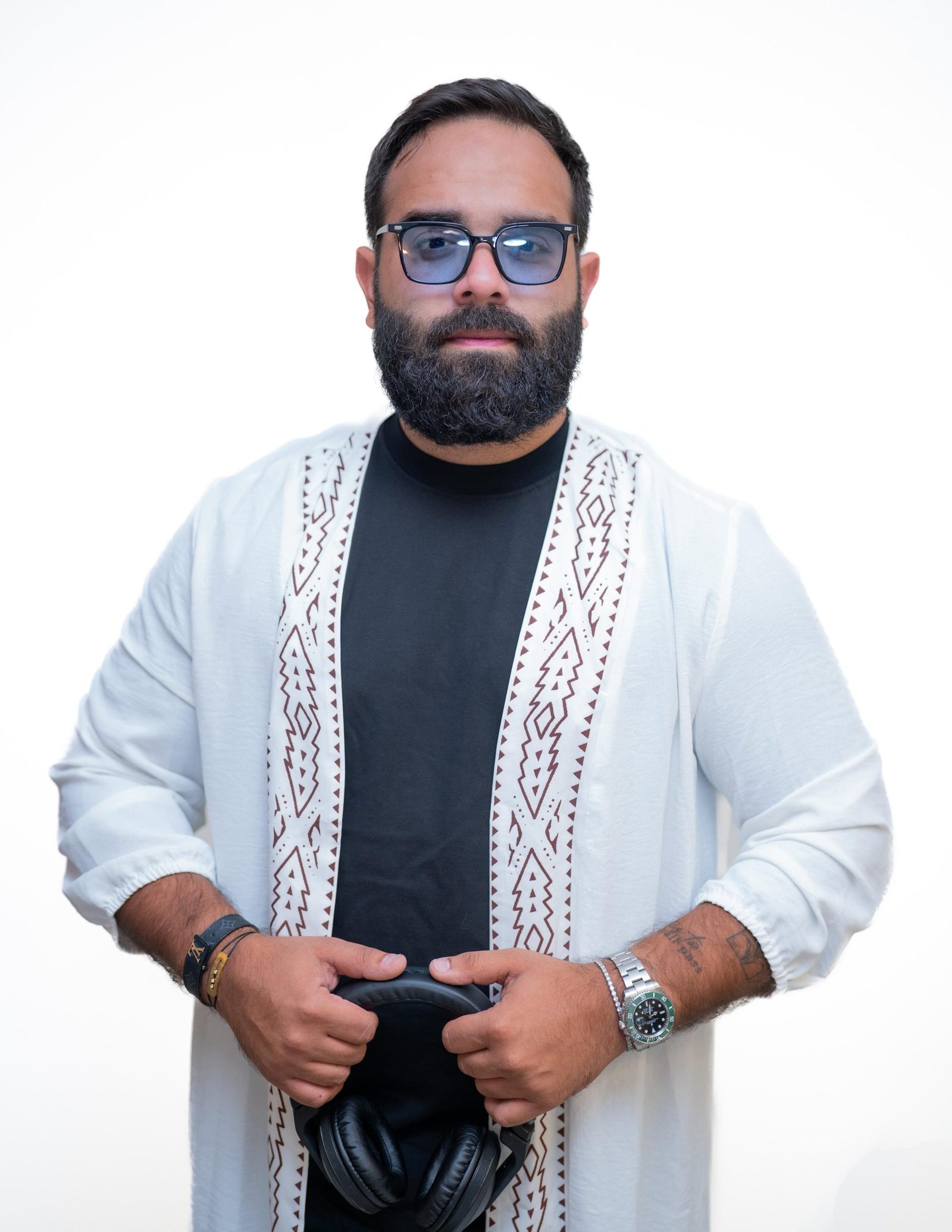 DJ LEMIR in a white thobe with maroon embroidered trim, holding a pair of headphones in both hands.