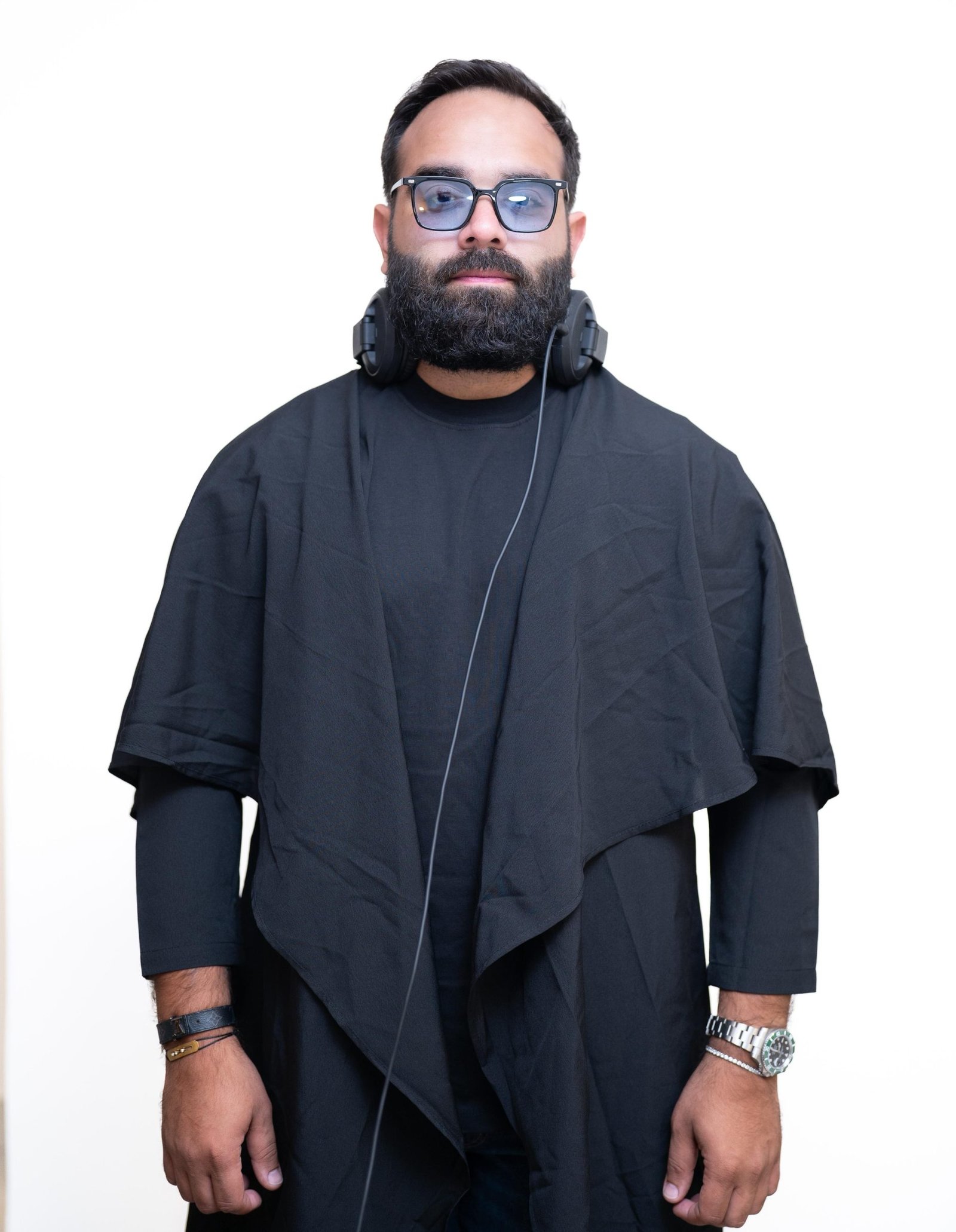 DJ LEMIR in a black draped thobe and glasses, headphones around the neck, against a pale backdrop.